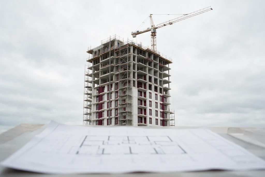 Prédio em construção com andaimes e guindaste, e planta baixa em primeiro plano