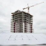 Prédio em construção com andaimes e guindaste, e planta baixa em primeiro plano