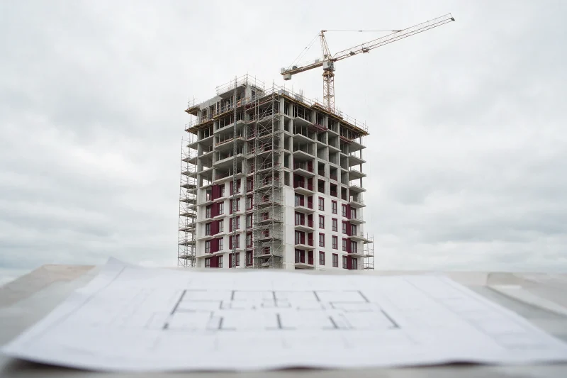 Prédio em construção com andaimes e guindaste, e planta baixa em primeiro plano